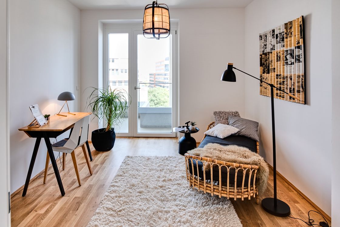 kleiner Holzschreibtisch mit Stuhl, Teppich und Rattan-Gästebett mit Stehleuchte