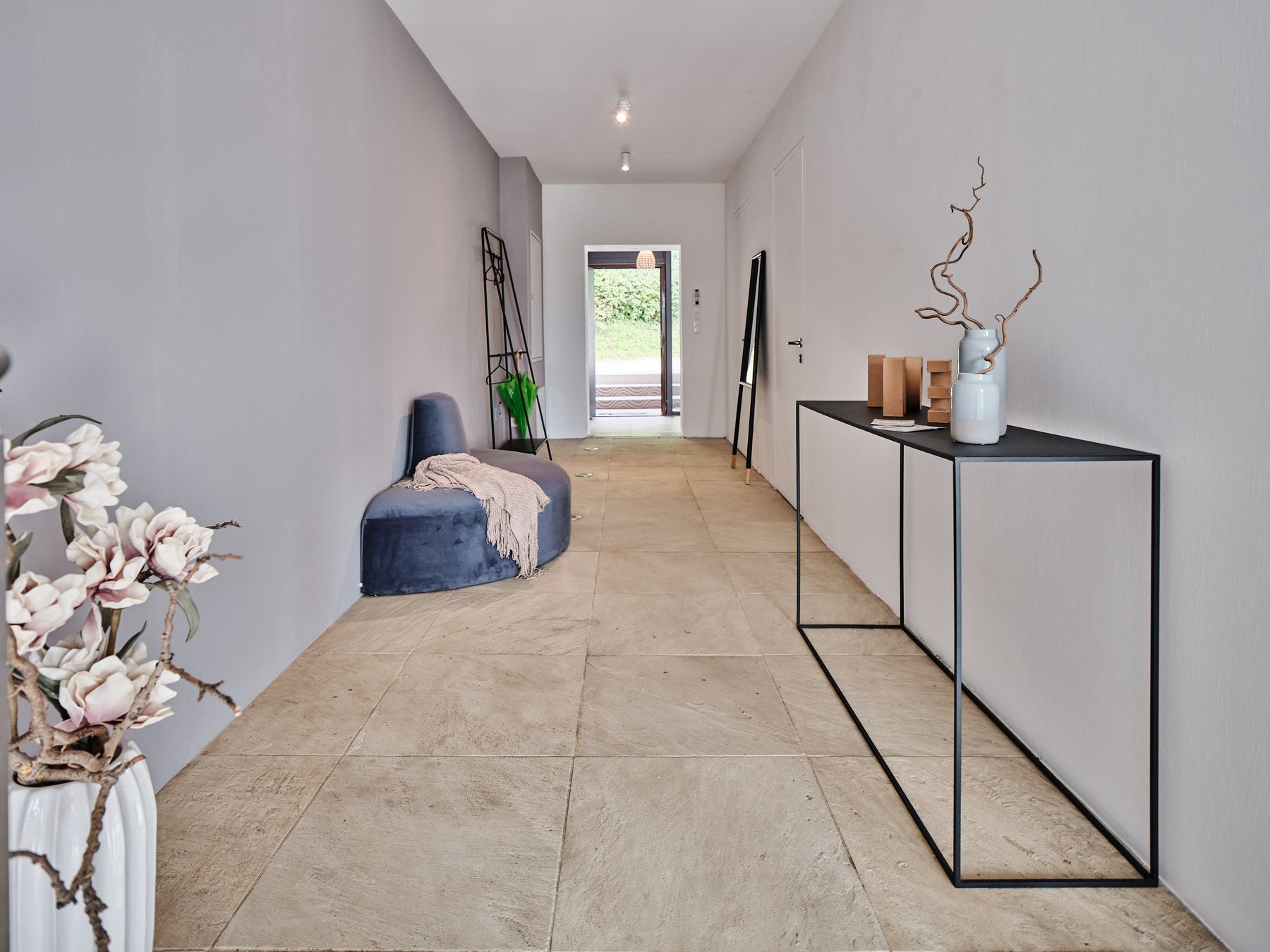 Langer Flur mit Steinboden und Samtbank in blau sowie Metallkonsole und Anlehngarderobe in Schwarz