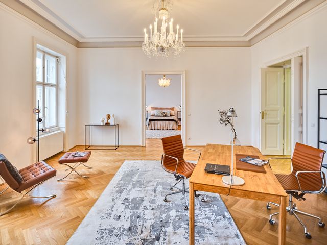 großer Raum mit Luster, Schreibtisch aus Holz, Ledersessel in braun und Teppich in grau