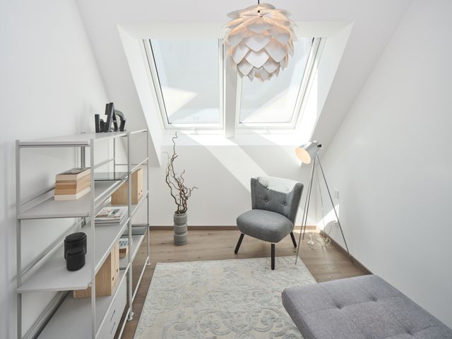 Gästezimmer mit grauem halbhohem Bücherregal, grauem Loungestuhl, silberner Schuppenleuchte, grauem Daybed und silbernem kurzflorigen Teppich