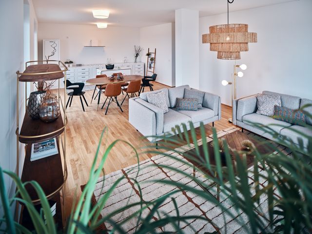 Blick vom Wohnzimmer Richtung Küche mit Esstisch oval aus Holz und 4 Polsterstühlen in braun und 2 Kunststoffstühlen in schwarz sowie 2 weißen schlichten Deckenleuchten