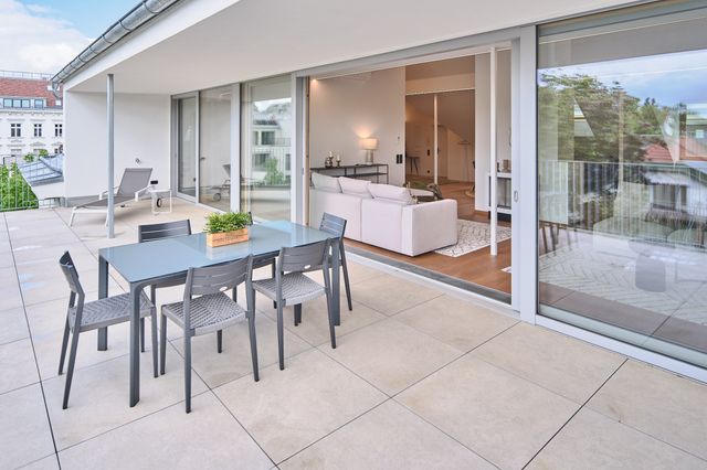 Terrasse mit Steinfliesen und grauem Esstisch samt grauen Stühlen - Blick ins Wohnzimmer