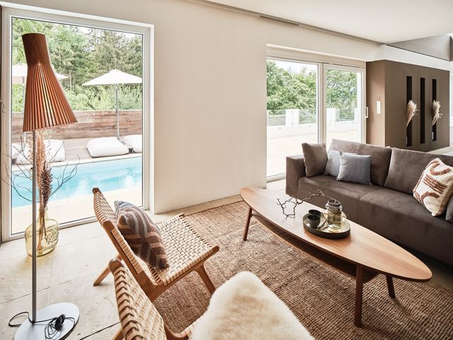 offener Wohnraum mit Blick auf die Pool-Terrasse, graues Samtsofa, Secto Stehleuchte aus Holzlamellen, Loungestühle aus Holz, ovaler Couchtisch aus Holz und Sisalteppich