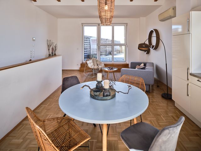Wohnzimmer mit Essbereich: graues Stoffsofa mit Augestell 2teilig, Sisalteppich, Loungestuhl aus Rattan, kleiner Beistelltisch aus Holz, Bogenleuchte mit Kartonschirm, Wanddeko aus Kartonkreisen, runder Esstisch Holz mit 4 unterschiedlichen Stühlen