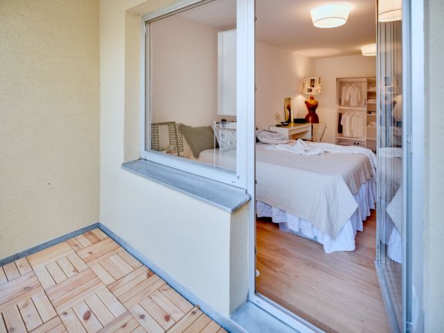 Blick vom Balkon ins Schlafzimmer mit Boxspringbett, weißer Schminktisch mit Metallstuhl, Stehleuchte aus alter Holz-Schneiderpuppe