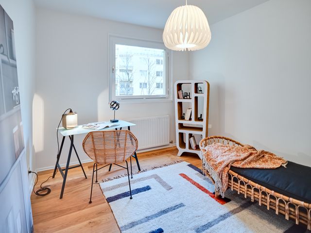 Jugendzimmer oder Gästezimmer mit kleinem Schreibtisch mit Bambusplatte, Rattan-Daybed samt Plaid und Kissen und einem nachhaltigen Karton-Regal und einem bunten Teppich